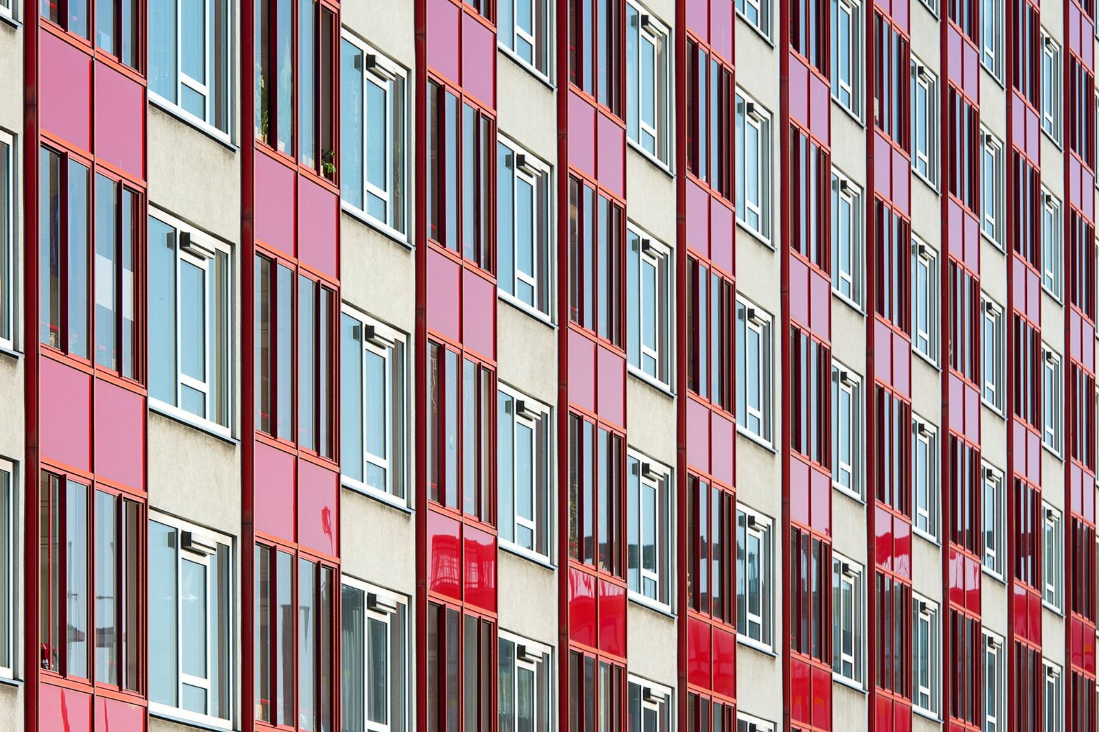 Apartment building facade with pink and red cladding panels and rows of windows