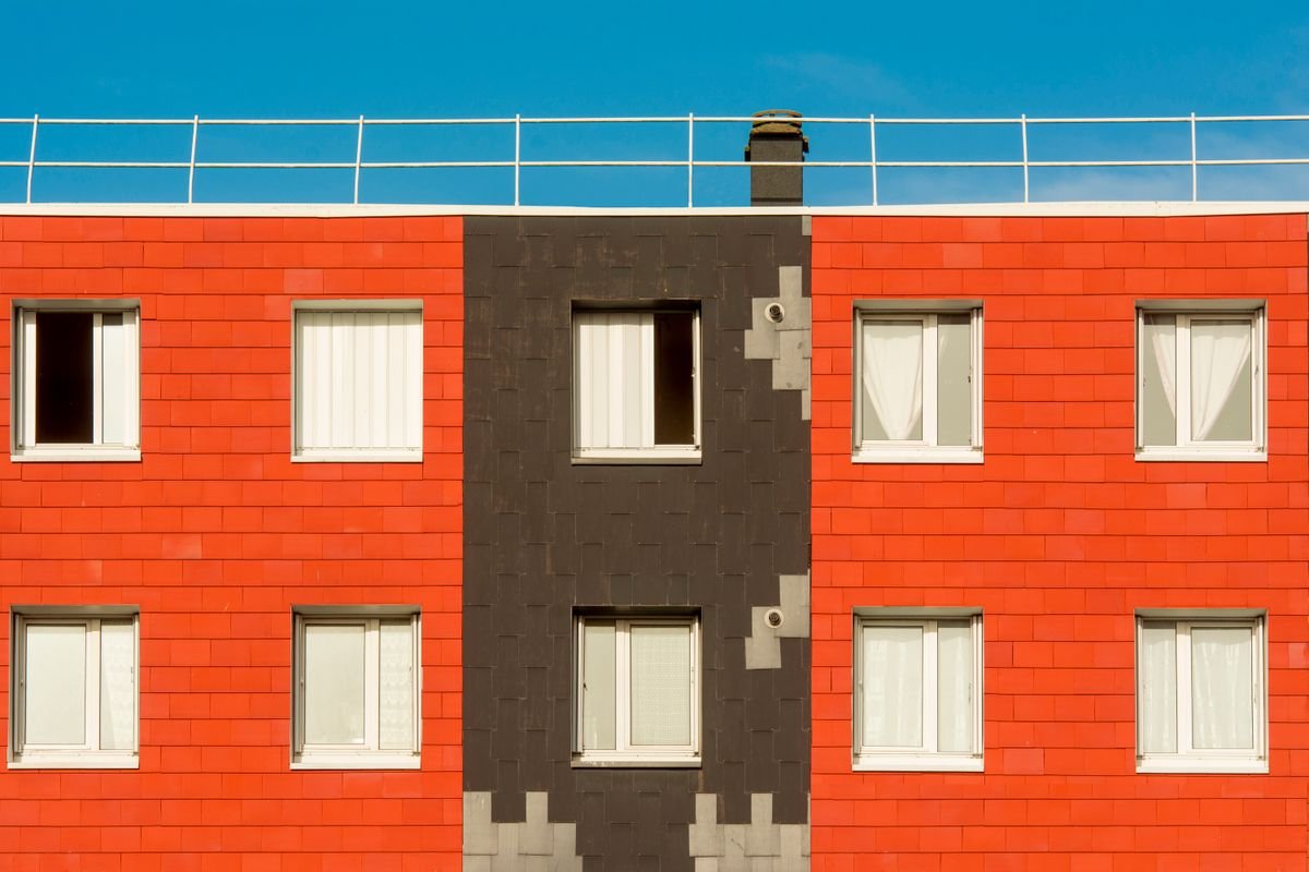 Building facade with orange-red panels, dark brown sections, and white-framed windows