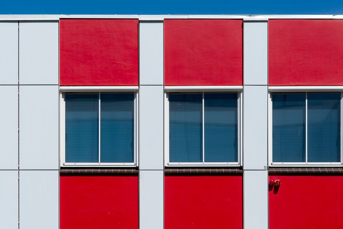 Contemporary building facade with red and white panels and windows under a clear blue sky