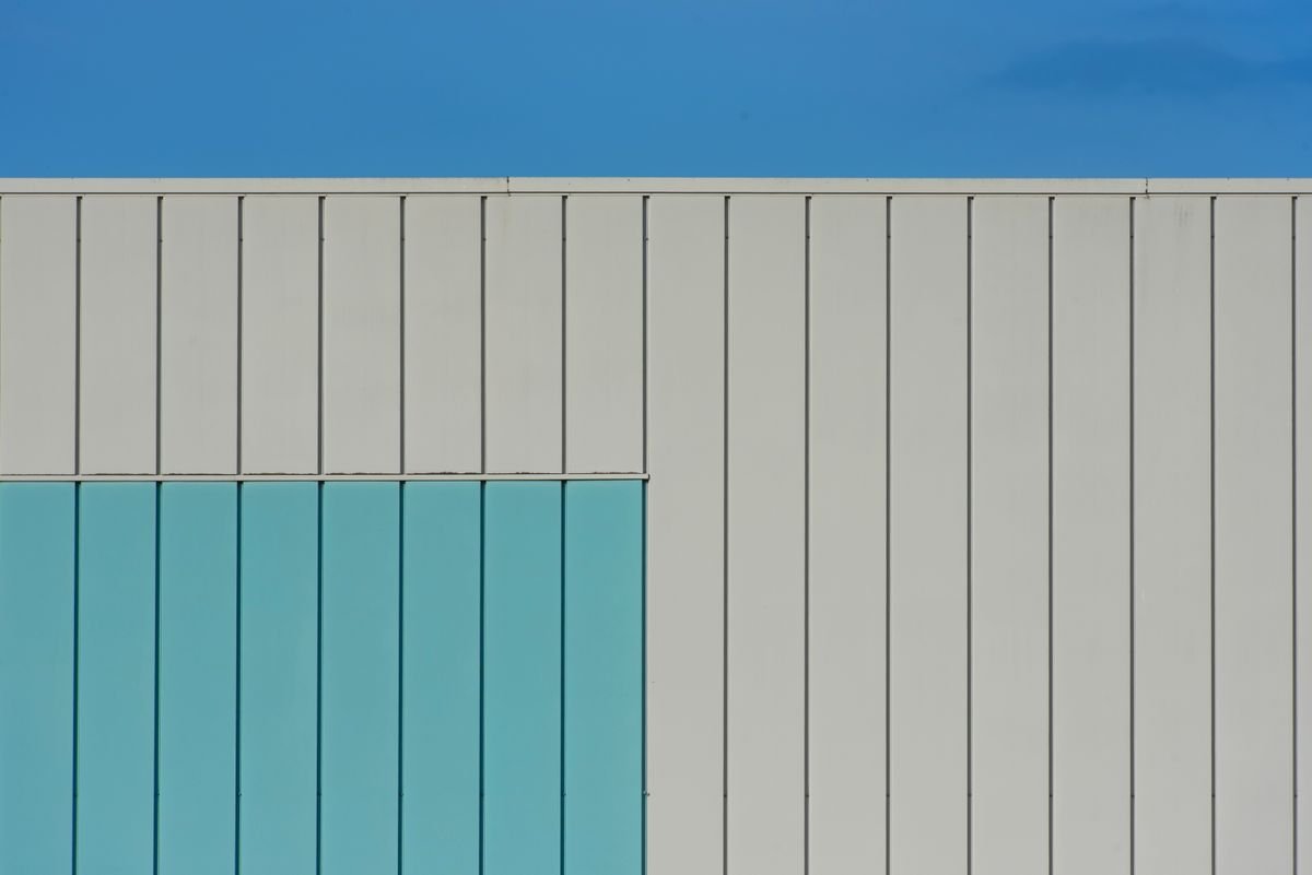 Modern minimalist building facade with geometric design and blue accents under a clear sky