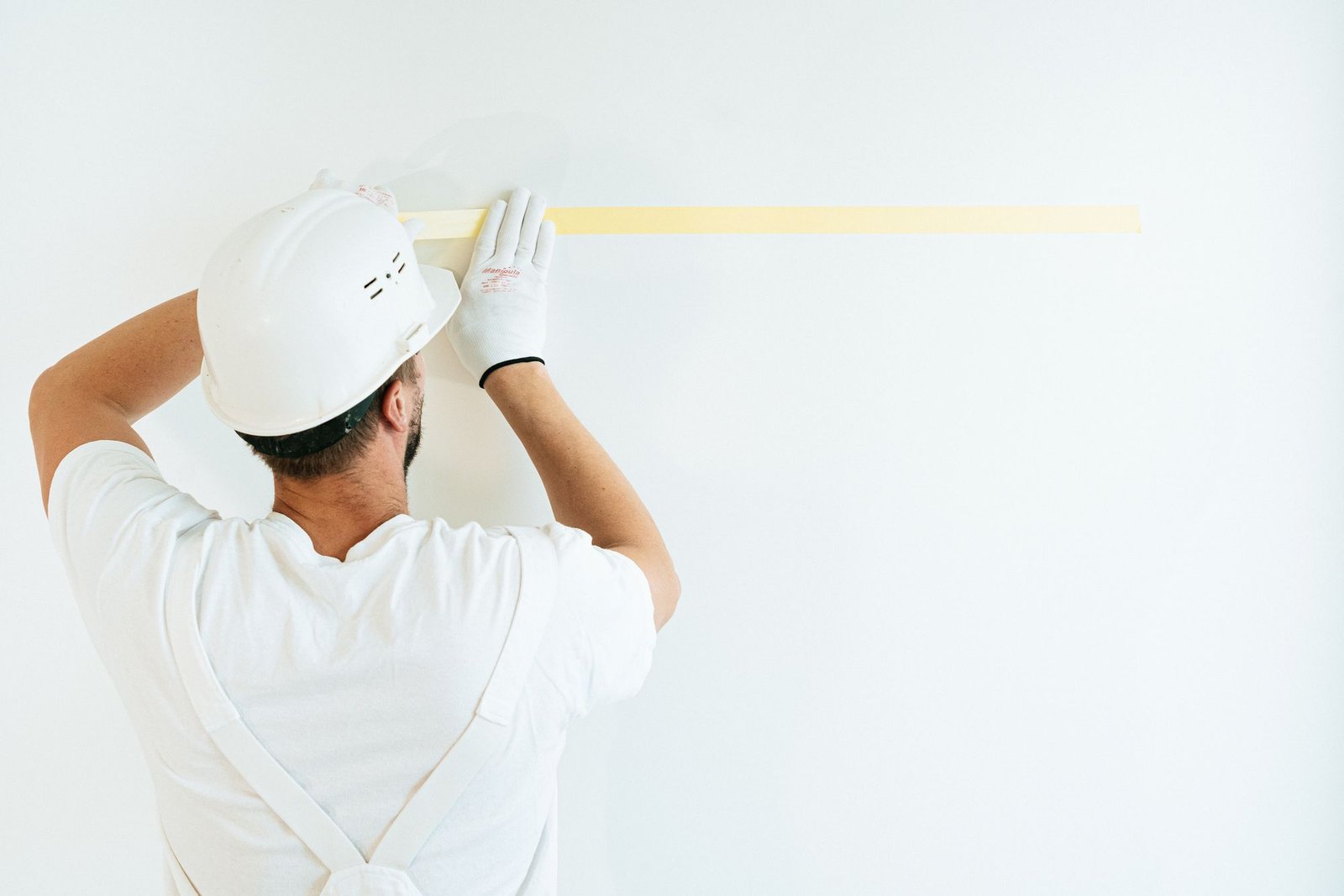 Technician in a hard hat marking a wall with a tape measure in a bright empty room