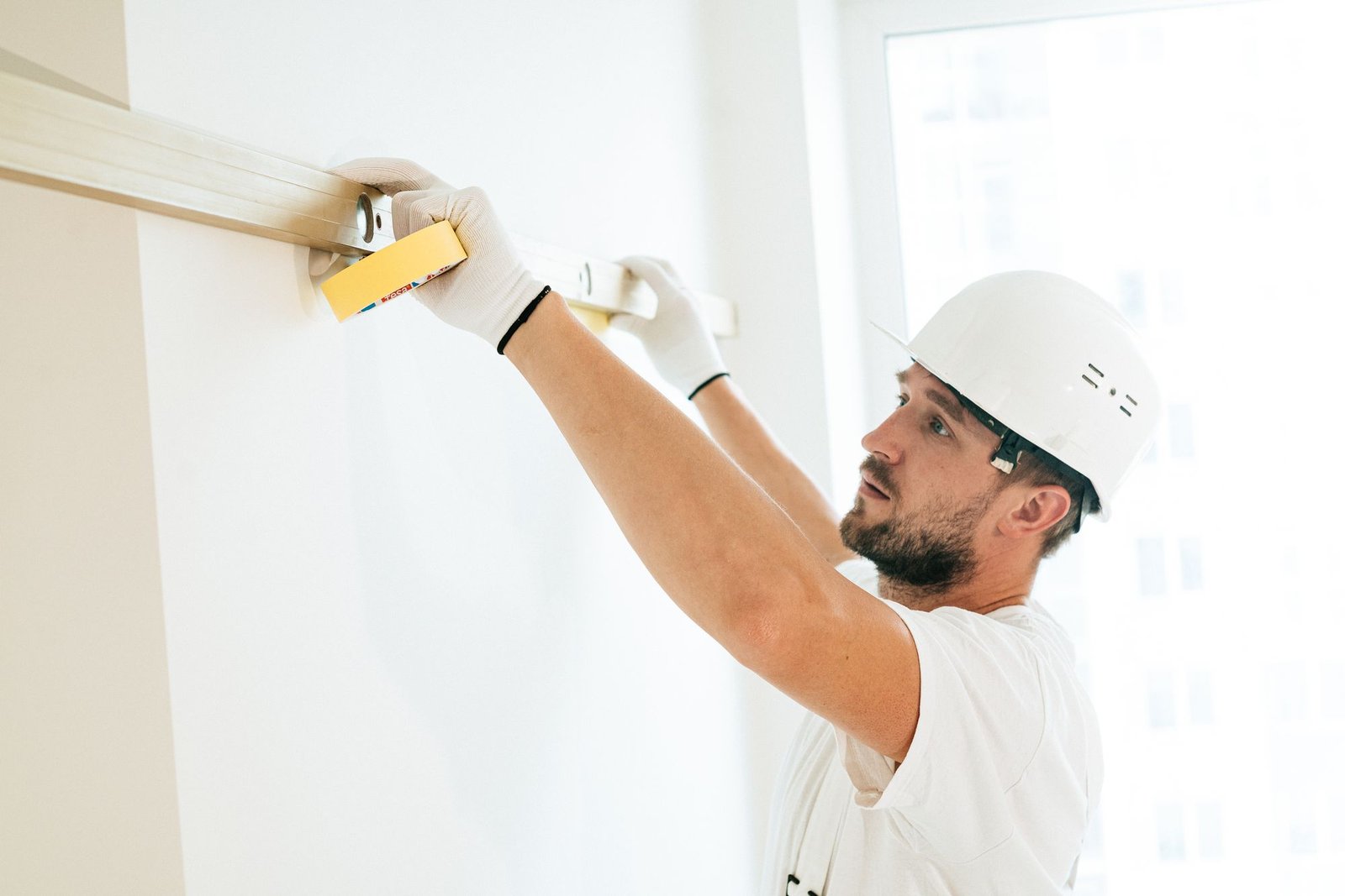 Technician in a hard hat marking a high level line on a wall with a tape measure