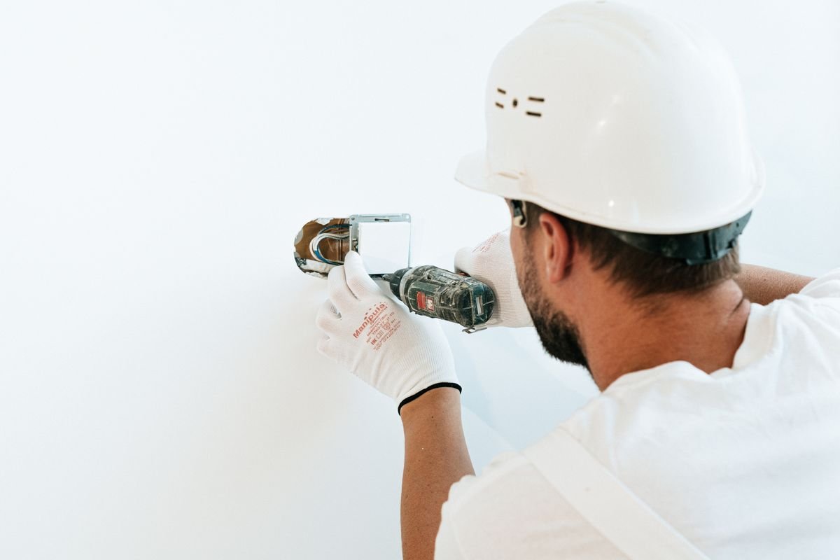 Technician in a hard hat drilling fixings into a wall
