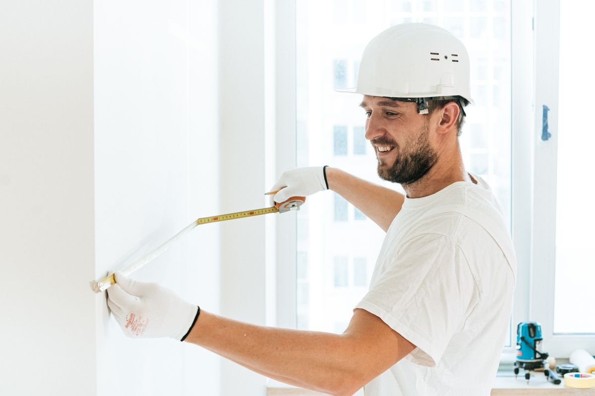 Technician in a hard hat measuring a wall with a tape to set out levels