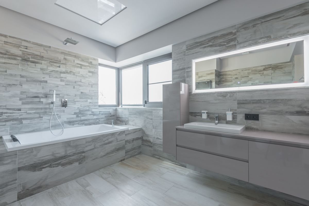 Fitted bathroom with stone-effect wall tiles, a freestanding bath, and an illuminated mirror
