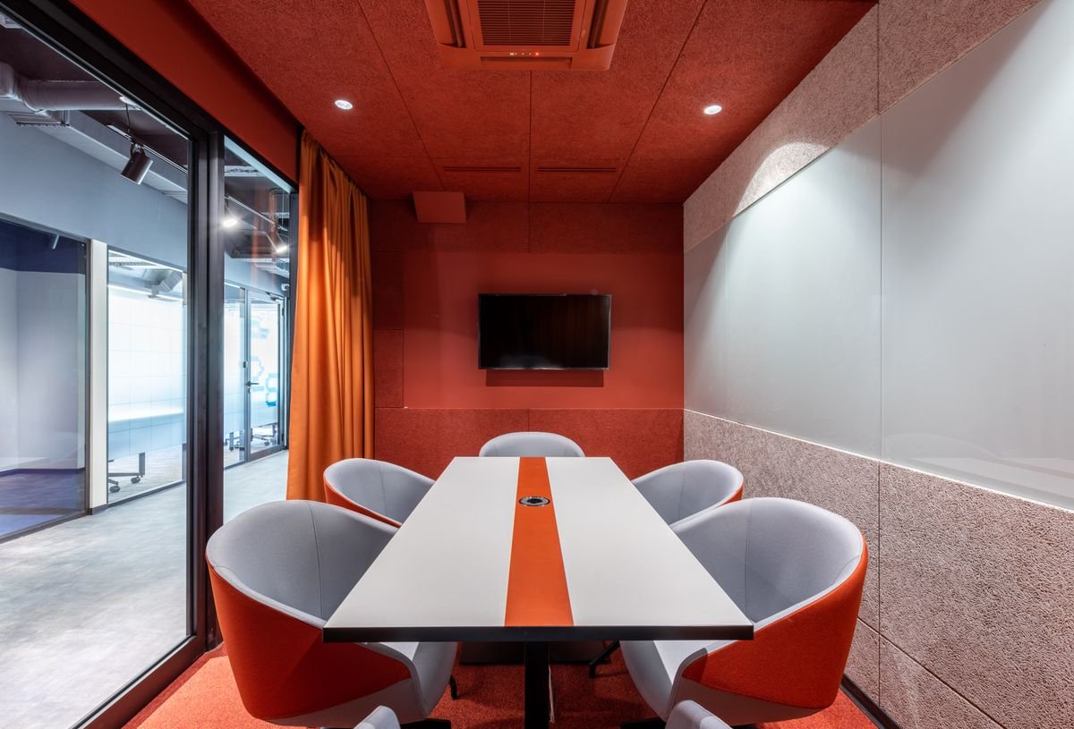 Meeting room fit-out with red acoustic walls, orange curtains, and a glass front