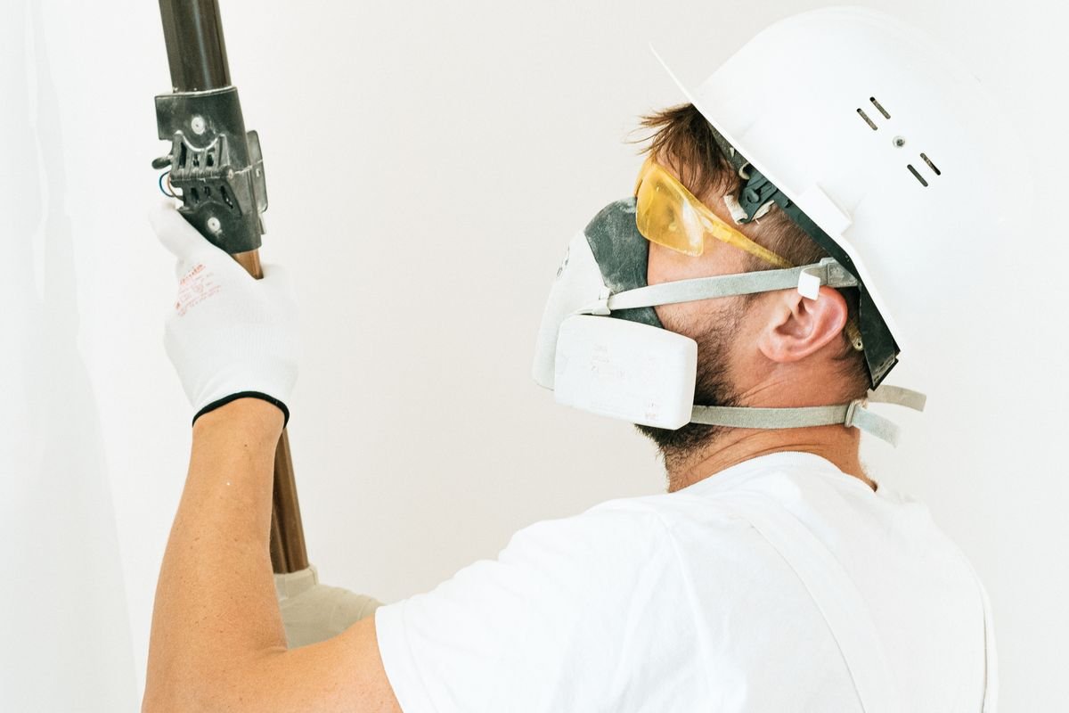 Technician wearing a dust mask and hard hat drilling into a wall