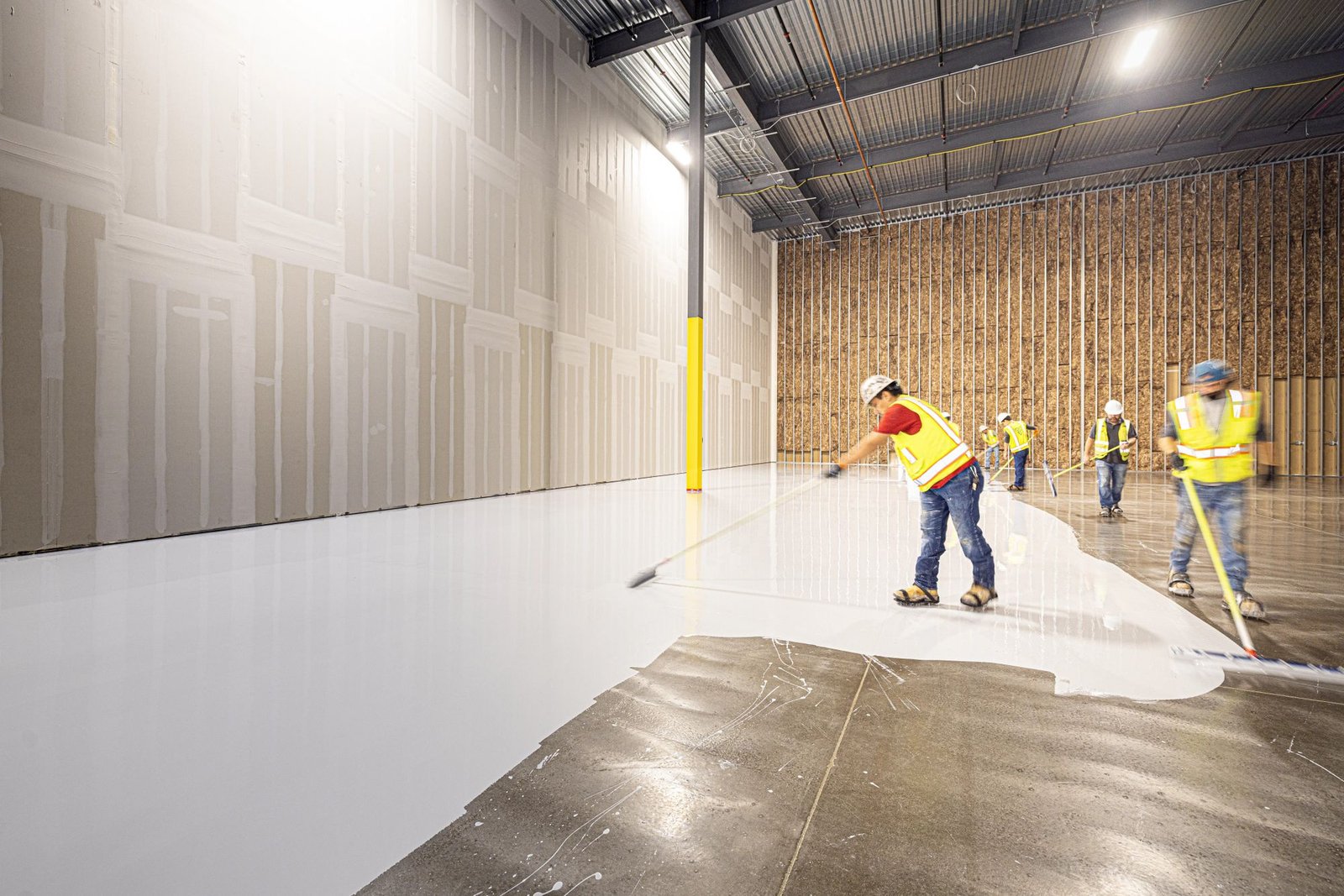 Construction crew applying epoxy flooring in a large commercial warehouse space