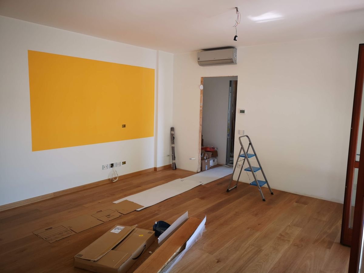 Bright empty room under renovation with ladder, tools, and wooden flooring