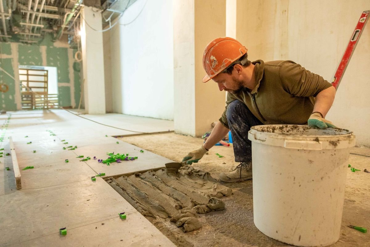 Construction worker laying tile in a renovation project wearing safety gear
