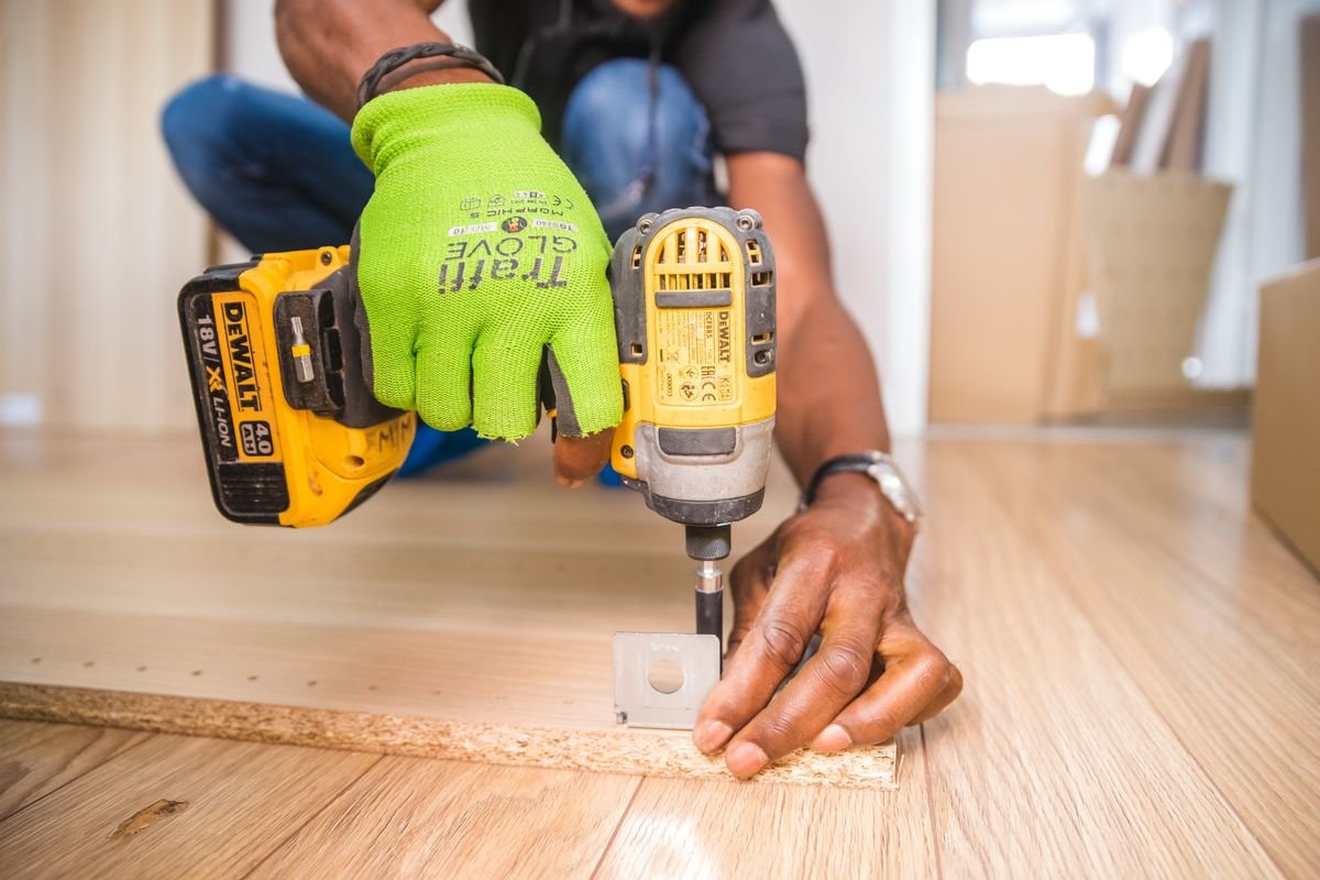 Person using a power drill for home improvement on a wooden floor
