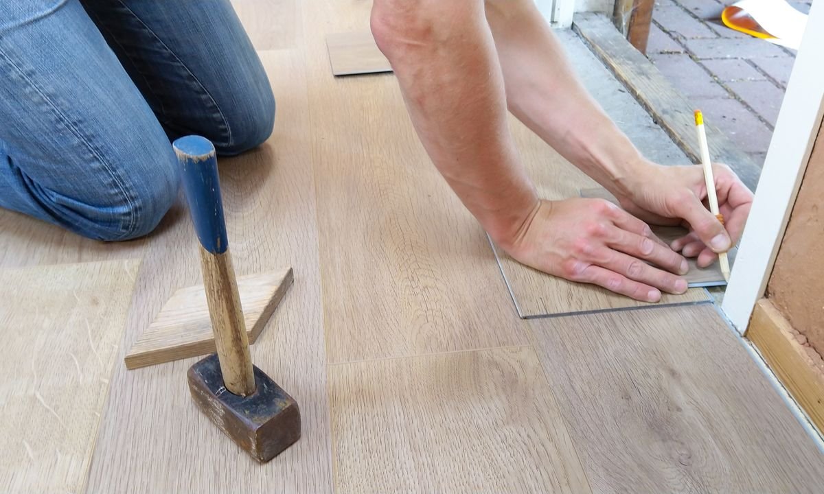 Craftsman measuring and marking wooden floor panels for precise installation