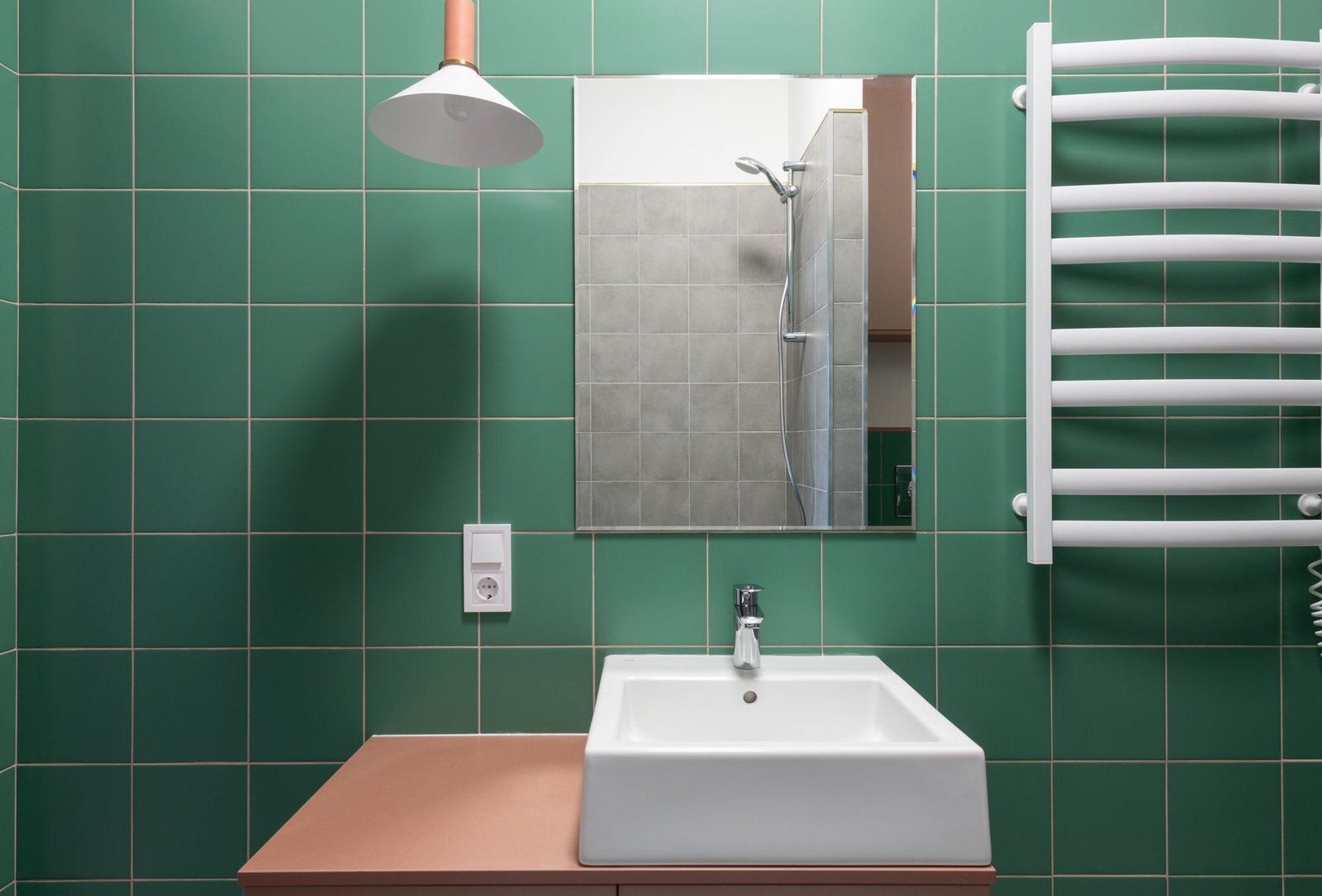 Bathroom wall tiled in deep green ceramic with a white basin and heated towel rail