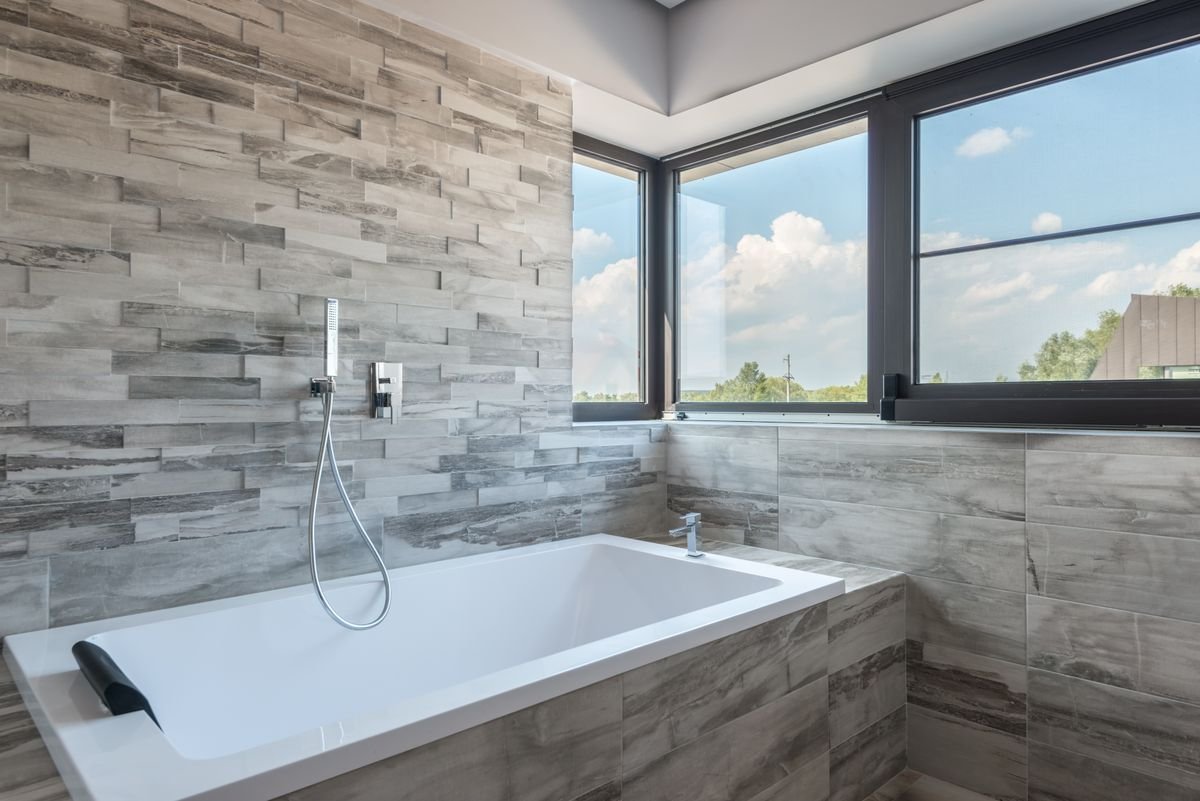 Bathroom with stone-effect grey wall tiles, a bathtub, and a large window