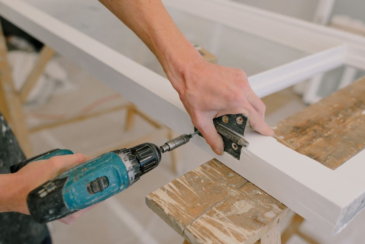 Professional installing a metal hinge on a wooden window during repair