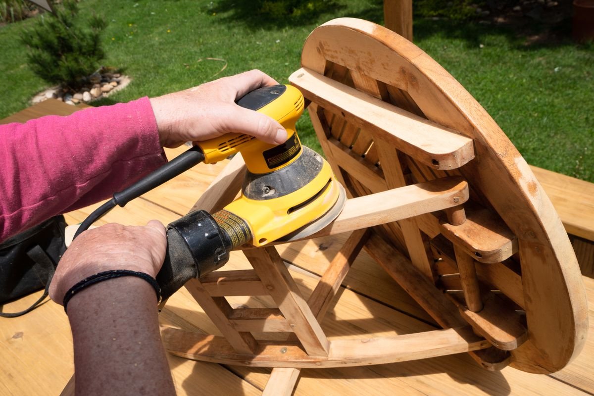Person using a power sander on a wooden table