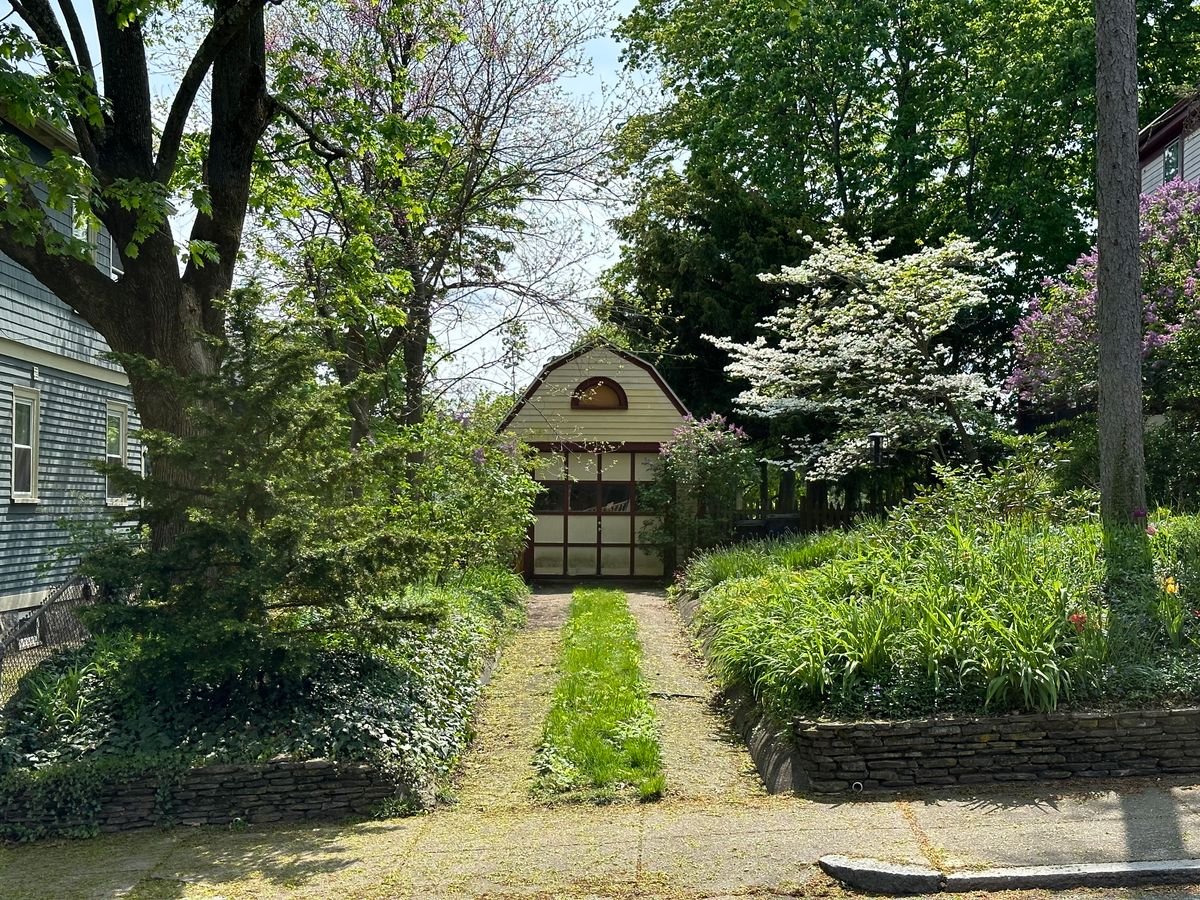 Paved garden path leading to a small garden building between planted borders