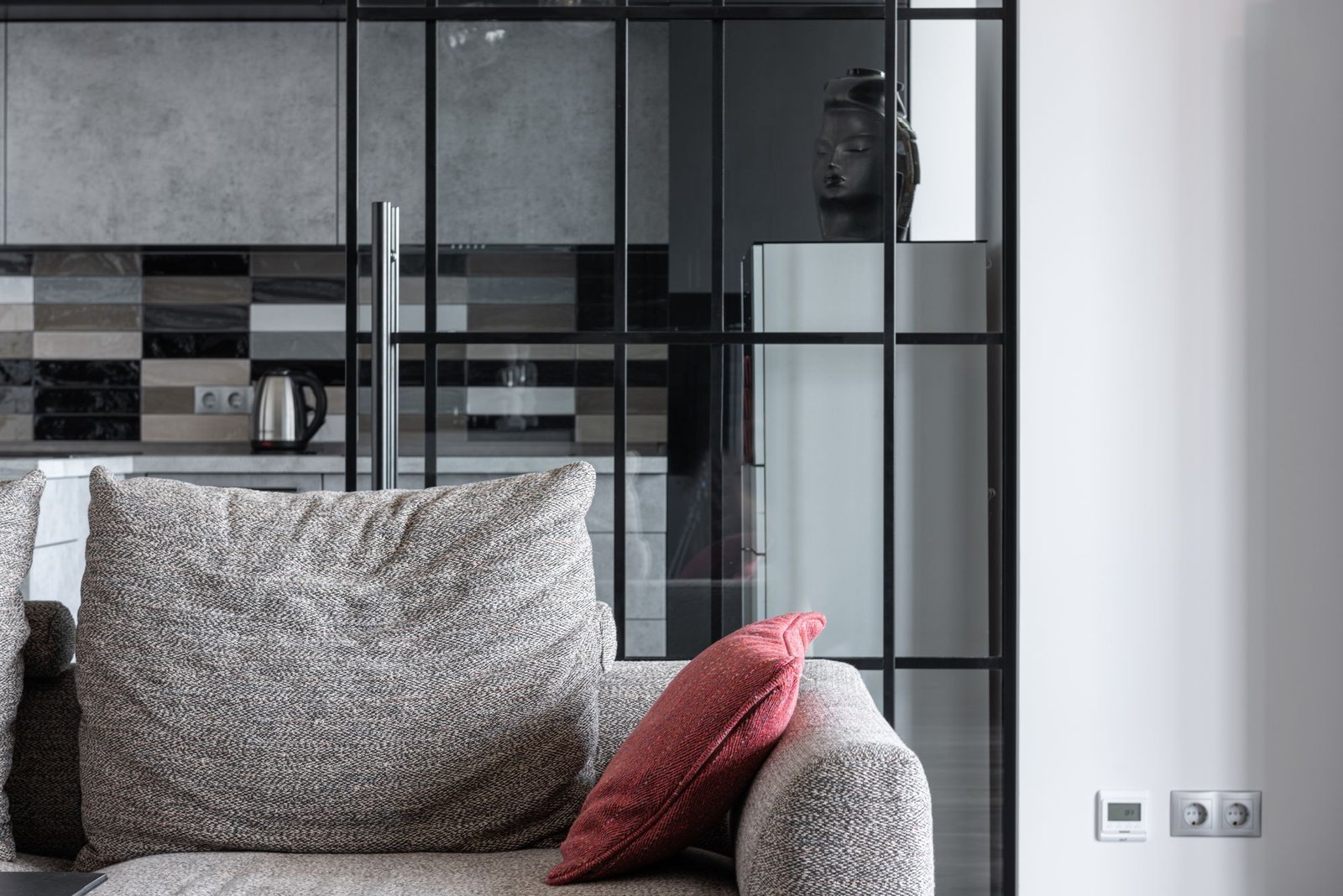 Cosy living room with a textured sofa and red cushion against a partition wall to a modern kitchen