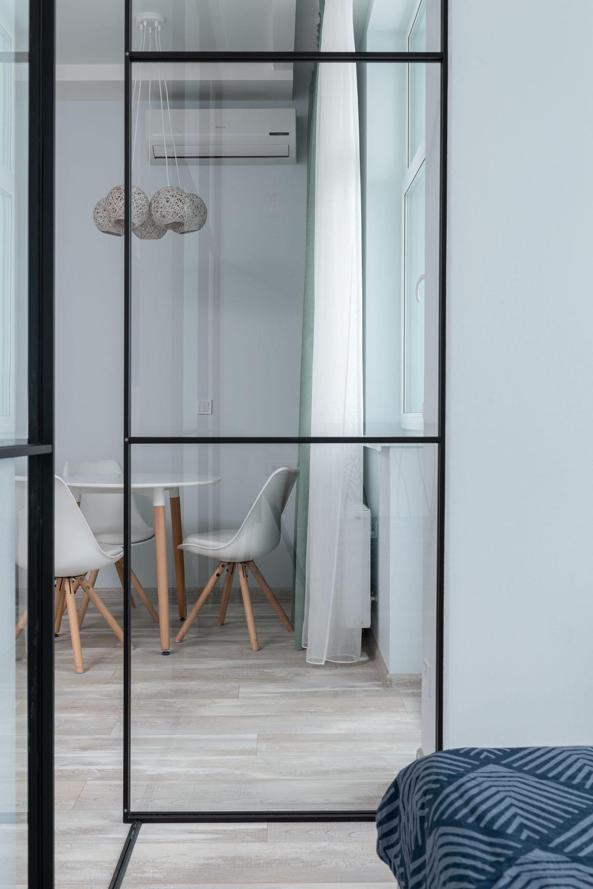 View of a round white table with chairs through a glass wall from a bedroom