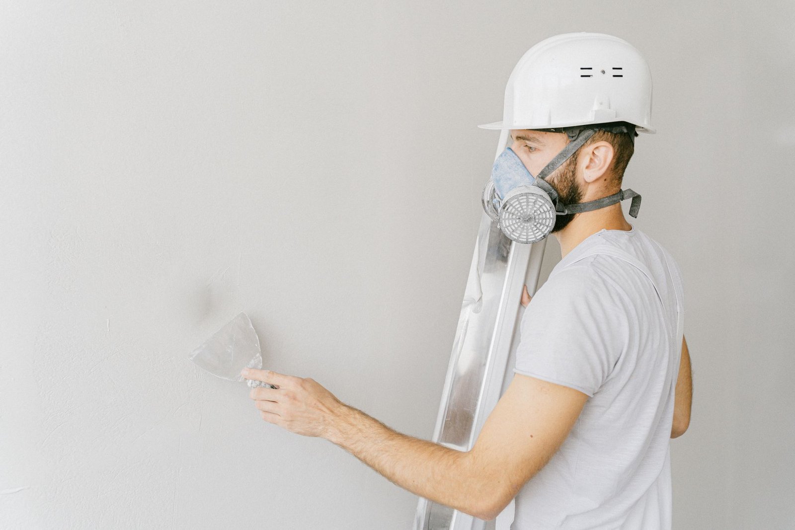 Plasterer in hard hat and respirator applying plaster to an interior wall with a spatula