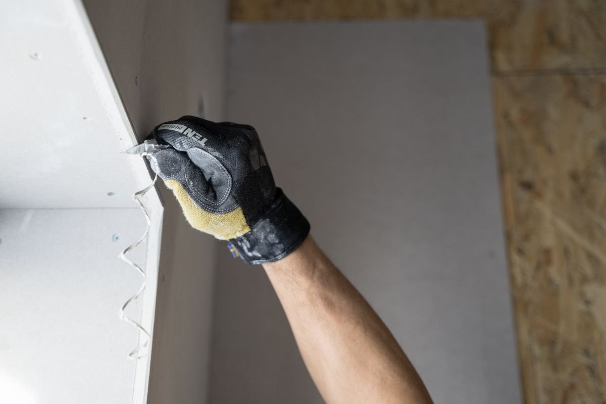 Gloved hand applying plaster to a plasterboard edge