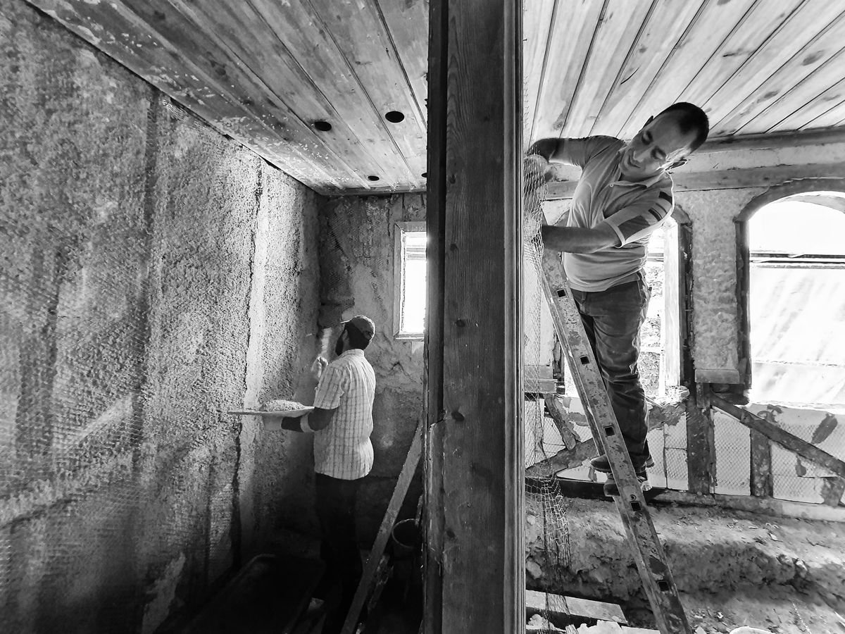 Two workers repairing plaster on a damaged old interior wall, one on a ladder