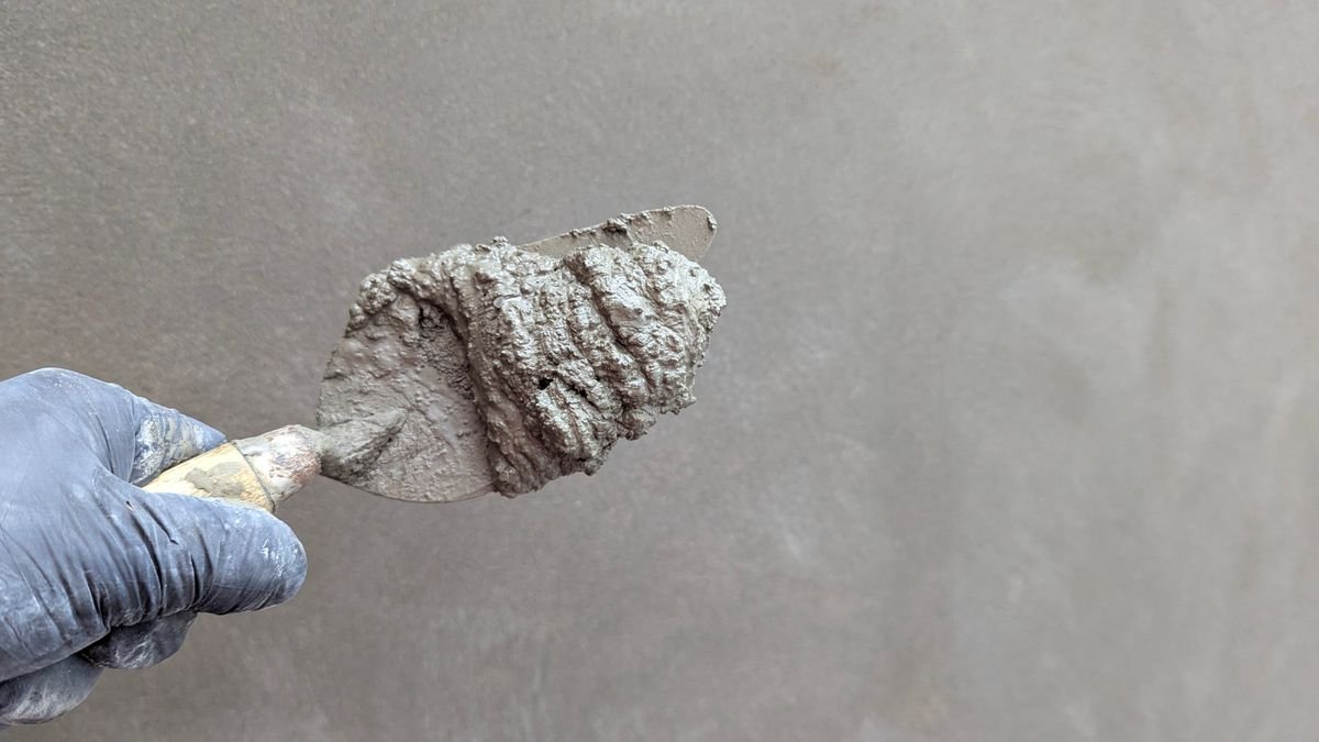 Gloved hand holding a trowel loaded with fresh plaster against a wall
