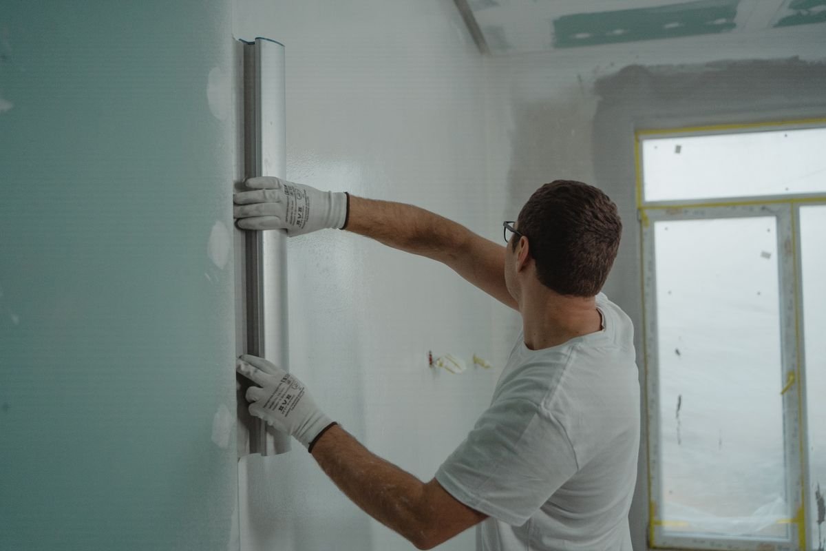 Worker in gloves levelling a plastered wall with a metal straightedge