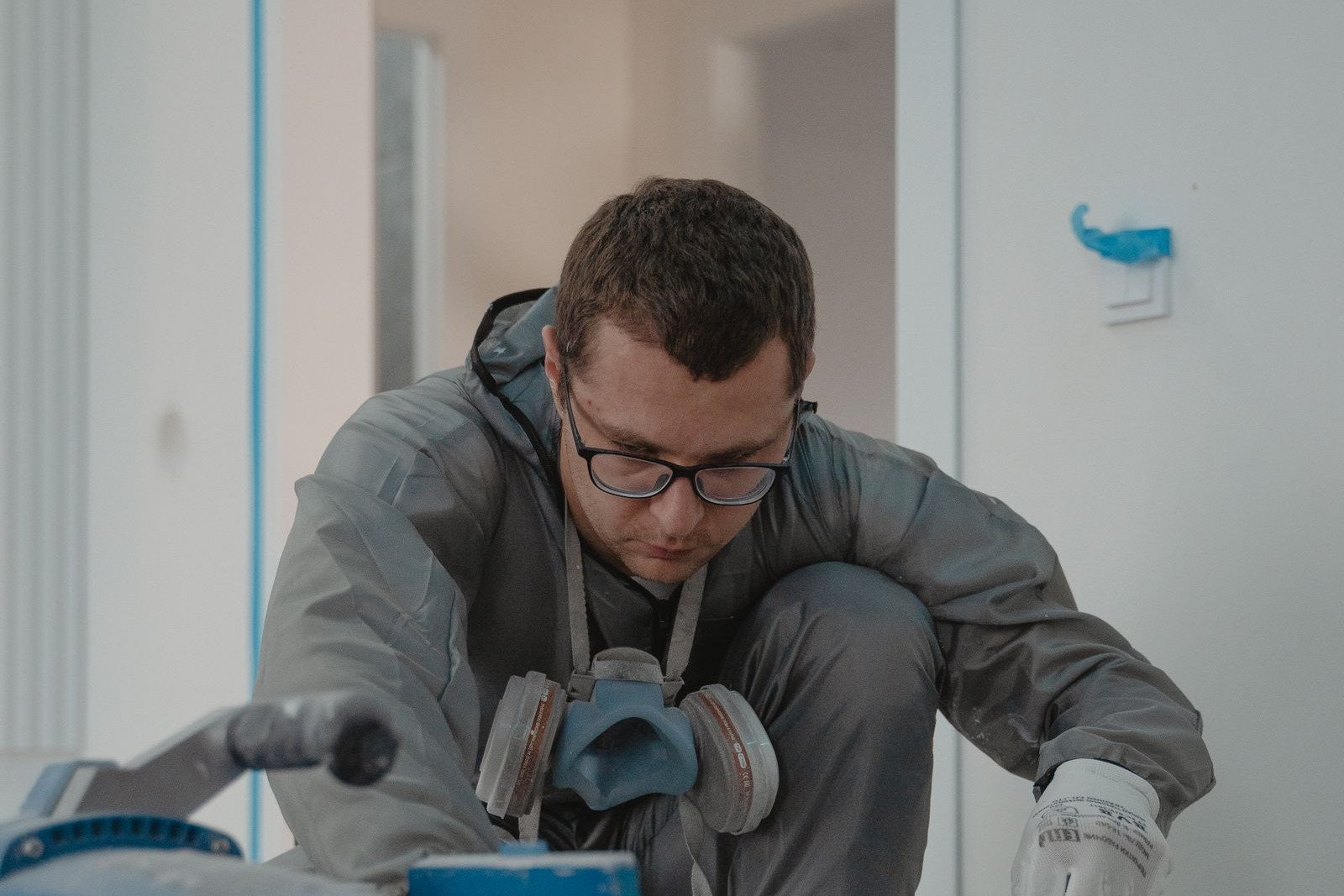 Painter in protective coveralls and a respirator working beside spraying equipment