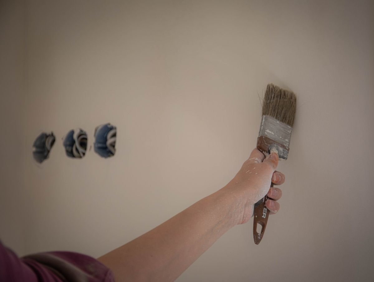 Painter using a brush to cut in around wall fixtures with precision