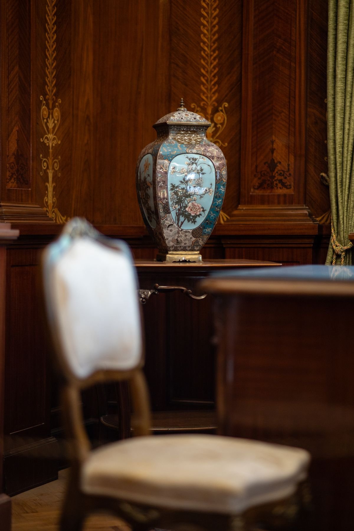 Antique decorative vase on a wooden table beside an upholstered chair