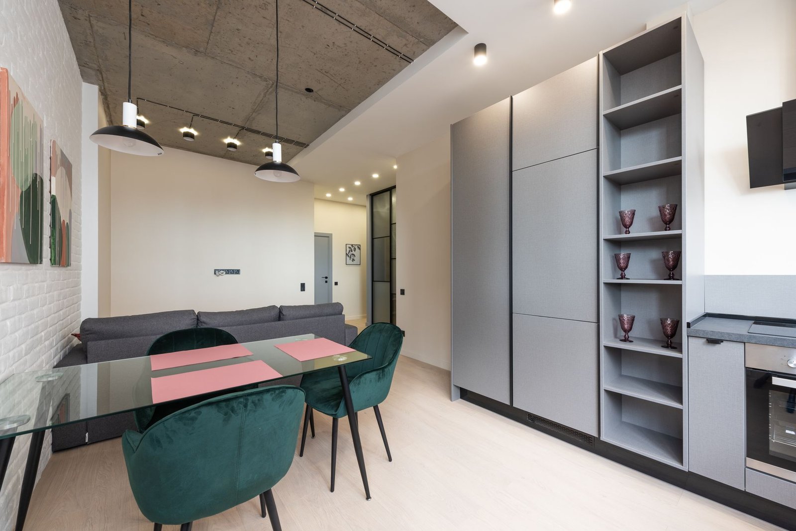 Apartment interior with a concrete ceiling, green velvet dining chairs, and grey built-in cabinetry