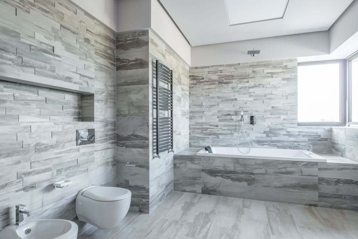 Bathroom with stone-effect grey wall tiles, a bathtub, and a heated towel rail