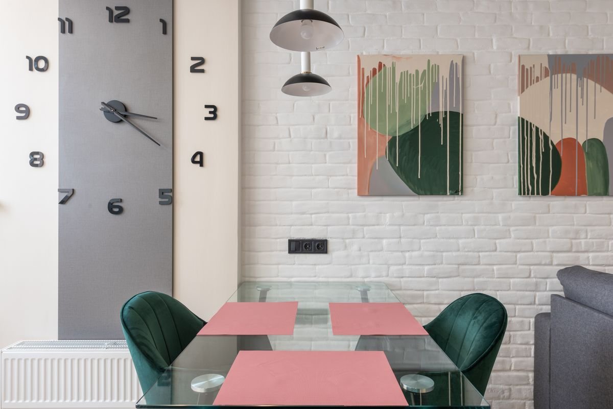 Dining area with a white brick wall, abstract artwork, and a large black wall clock
