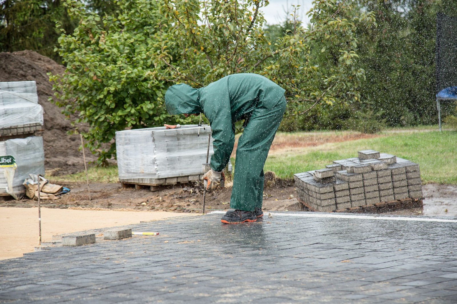 Worker in protective gear laying interlock paving stones outdoors
