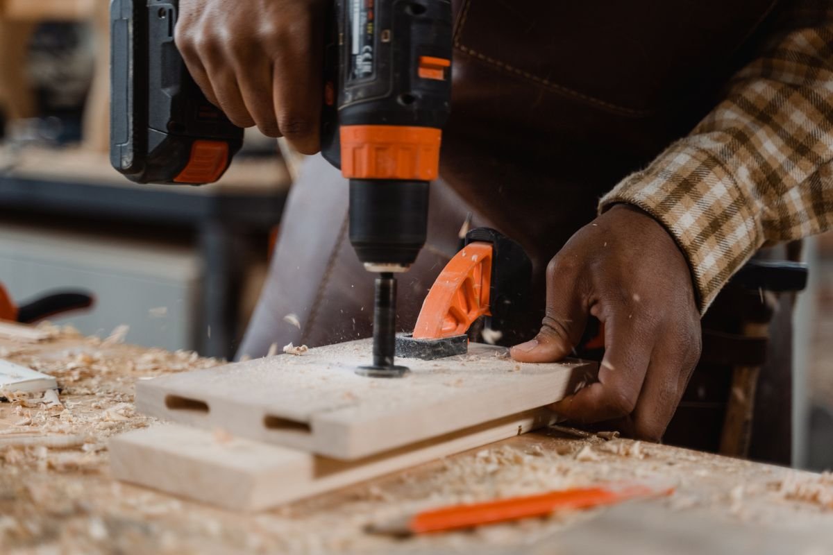Carpenter using a drill on wood, surrounded by sawdust