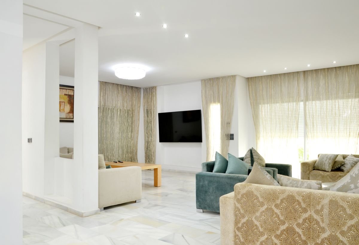 Bright living room with white marble floors, layered seating, and sheer drapes