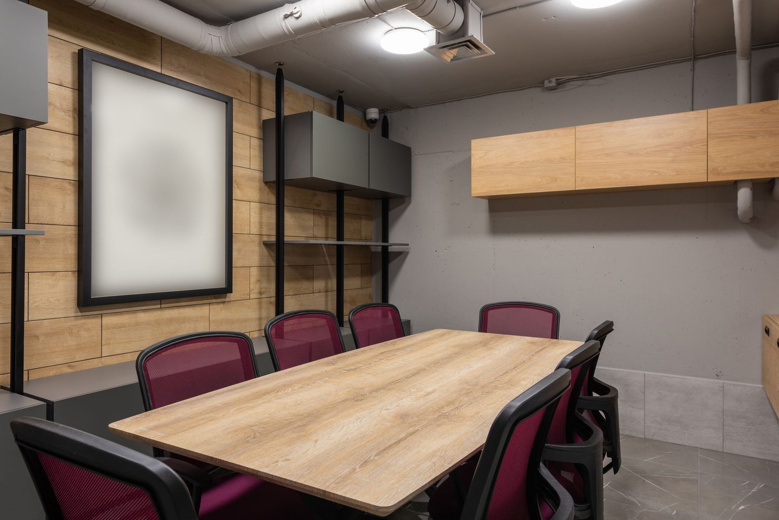 Meeting room with a timber table, burgundy chairs, and a large frosted glass whiteboard wall