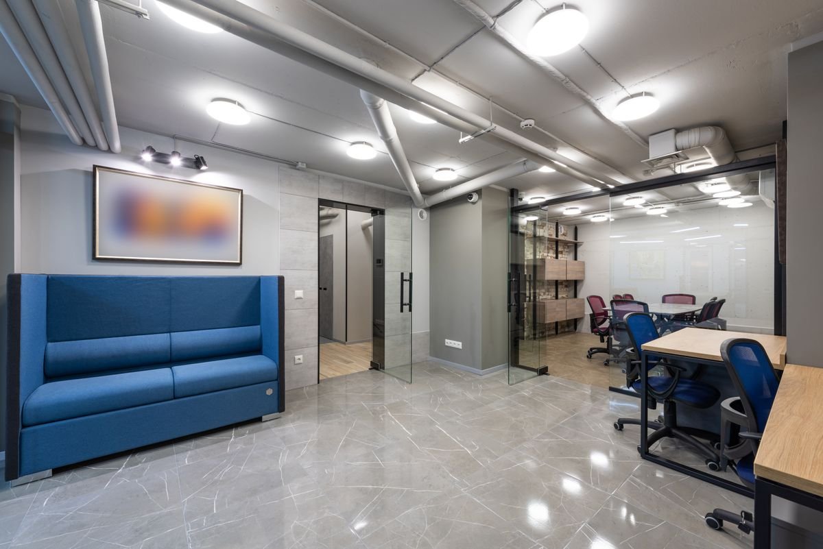 Blue sofa lounge area and desks in a bright office with a glossy floor