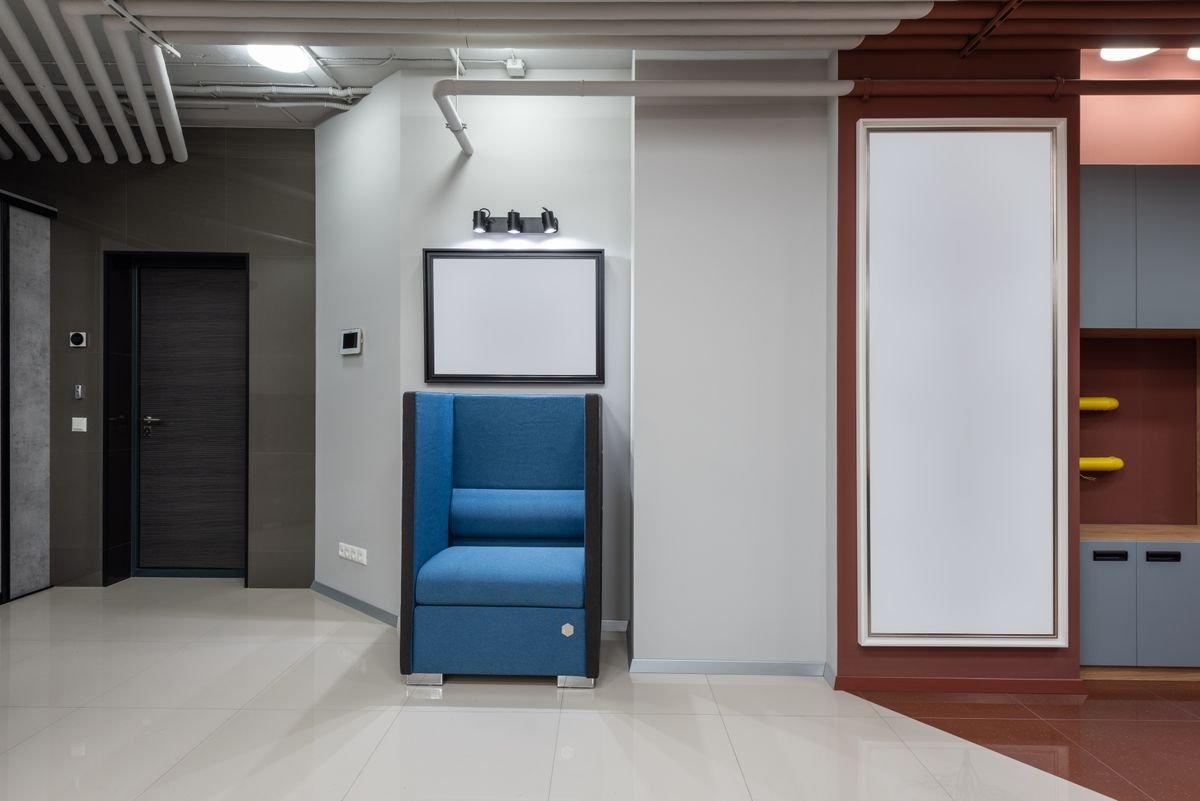 Blue seating pod and white board beside a dark door in an office corridor