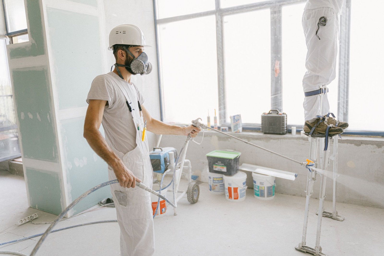 Uniformed painting crew in hard hats and respirators spraying interior walls of an apartment