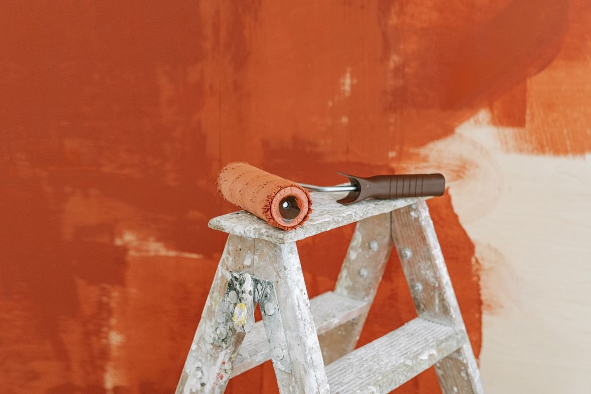Paint roller resting on a ladder in front of a partly repainted wall