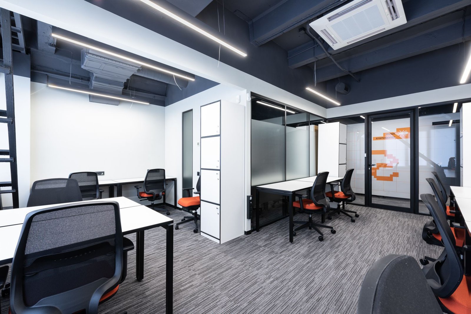 Open-plan office with white desks, blue task chairs, black exposed ceiling, and glass partitions