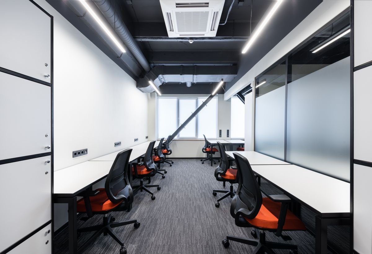 Open-plan workstations with orange task chairs under a black exposed ceiling