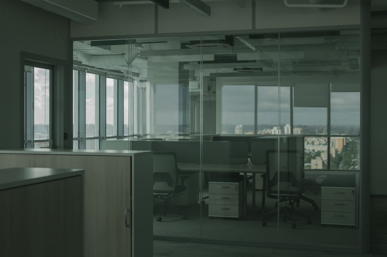 Empty modern office with glass partition walls, black chairs, and city views