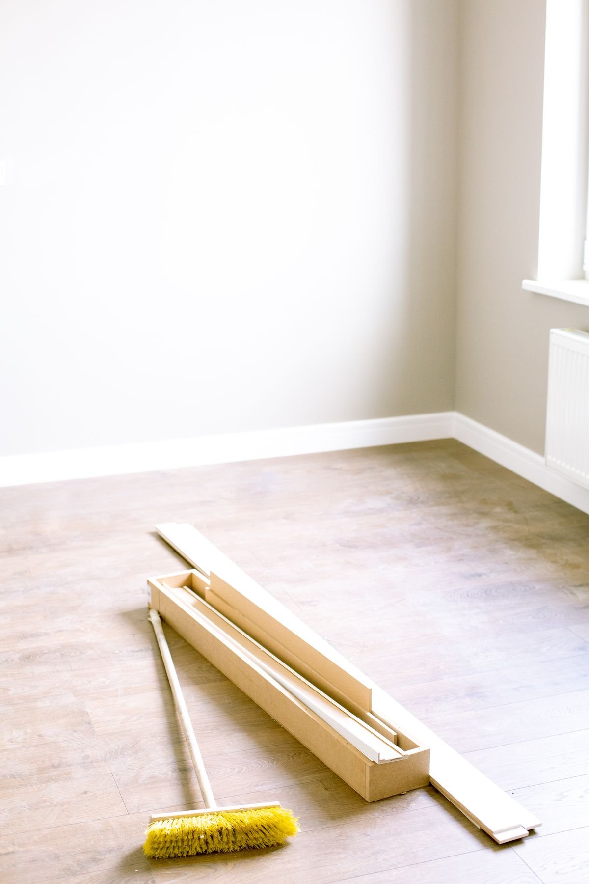 Empty room with stacked wood planks and a floor brush, ready for installation