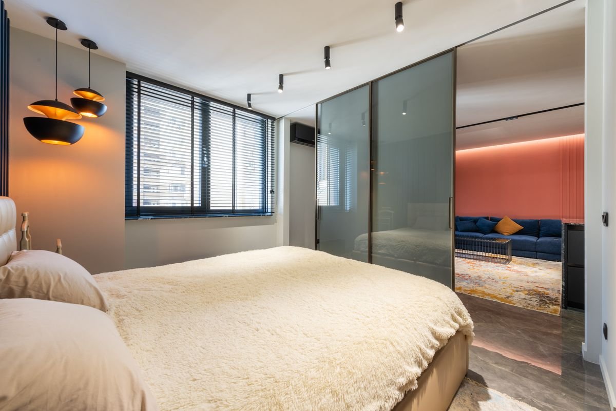 Bed with pillows and cover against a glass wall and window with lamps