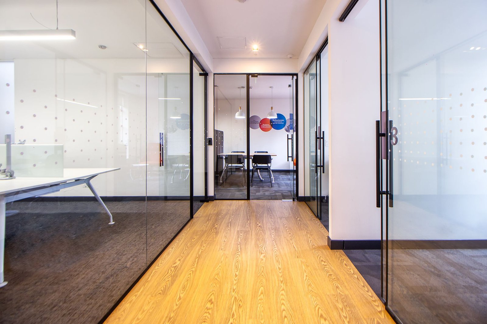Bright modern office hallway lined with glass walls leading to a conference room