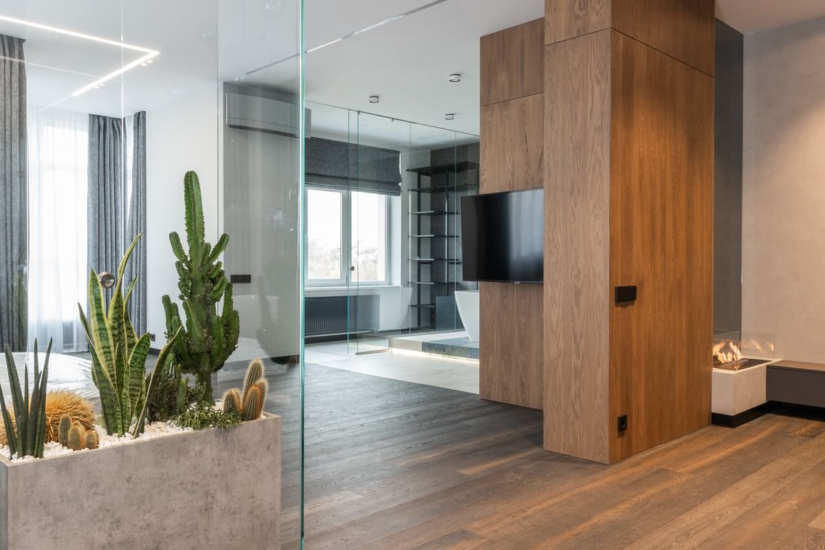 Spacious studio with a glass-walled box of tropical plants and a wooden floor