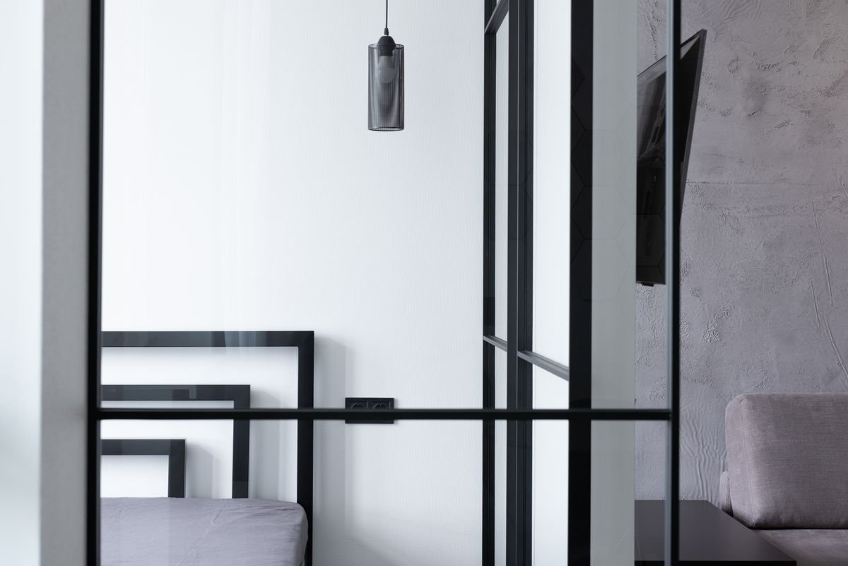 Bedroom and living room separated by a glass wall, with a hanging lamp and TV
